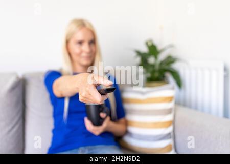 Frau, die die Fernbedienung verwendet, während sie zu Hause Fernsehen Stockfoto