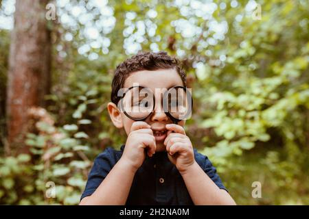 Netter Junge, der durch die Lupe im Wald schaut Stockfoto