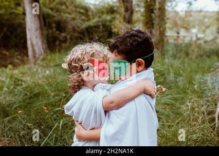 Jungen tragen Masken und Umhänge, die sich im Wald umarmen Stockfoto