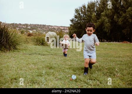 Junge läuft mit einem Freund, der Pappkarton trägt, während er auf der Wiese spielt Stockfoto