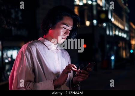 Hübscher junger Mann, der in der Stadt über das Mobiltelefon im Netz surft Stockfoto