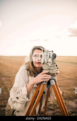 Reife Frau, die das Feld durch Theodolit misst Stockfoto