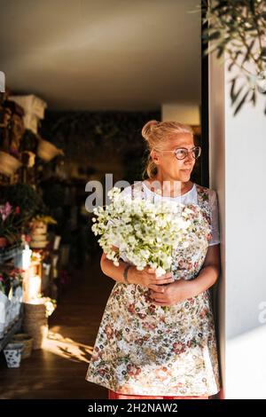 Reife weibliche Floristin mit blühender Pflanze, die Vase im Blumenladen wählt Stockfoto