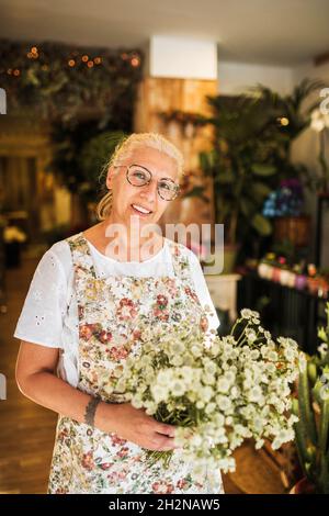 Nachdenkliche weibliche Floristin mit Blumen, die am Ladeneingang stehen Stockfoto