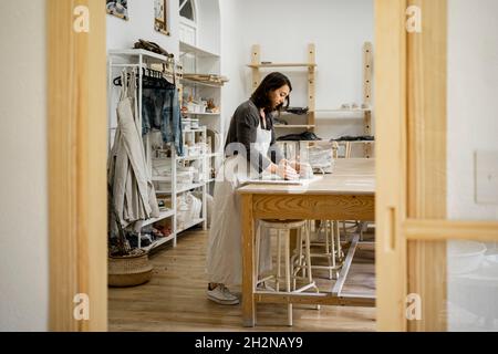 Junge Handwerkerin, die während der Arbeit in der Werkstatt Ton formt Stockfoto