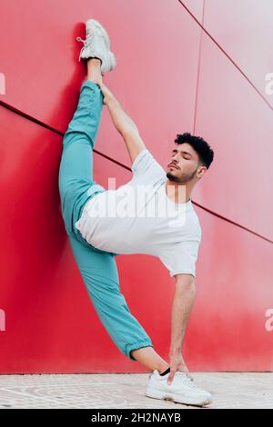 Männlicher Tänzer, der an der Wand lehnt und eine arabeske Position übt Stockfoto