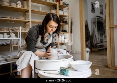 Junge weibliche Töpferin formt Ton während der Arbeit in der Werkstatt Stockfoto