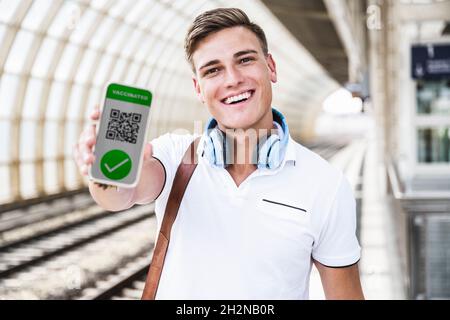 Glücklicher Mann, der am U-Bahnhof einen Impfpass auf dem Handy vorzeigt Stockfoto