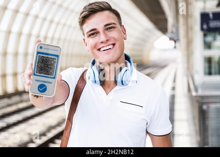 Lächelnder Mann mit Kopfhörern und Mobiltelefon mit Impfpass in der U-Bahn Stockfoto