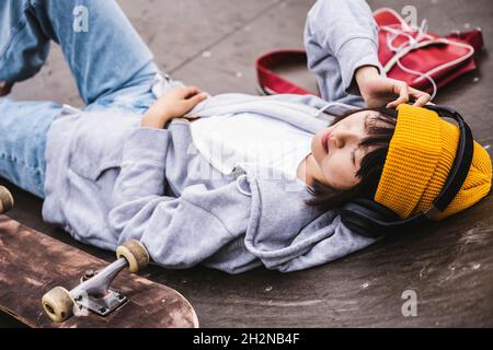 Teenager mit kabellosen Kopfhörern, die sich im Skateboard-Park ausruhen Stockfoto