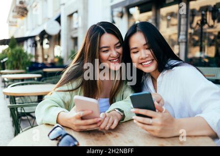 Glückliche Freundinnen, die Smartphones im Straßencafé benutzen Stockfoto