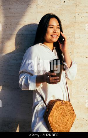 Glückliche Frau in einer Umhängetasche, die an der Wand auf dem Mobiltelefon spricht Stockfoto