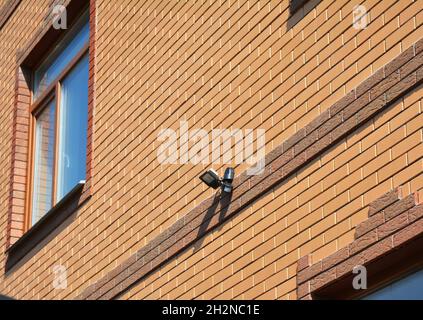 Motion Flood LED-Licht auf Haus Ziegelwand im Freien. Auswählen und Installieren der Bewegungsmelderbeleuchtung. Bewegungssensor. Stockfoto