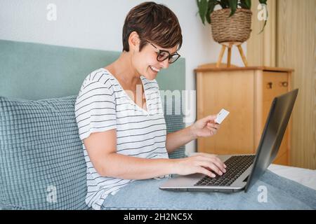 Glückliche Frau, die kontaktlose Zahlung per Kreditkarte macht, während sie zu Hause einen Laptop benutzt Stockfoto