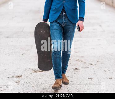 Ein selbstbewusster Geschäftsmann hält Skateboard und spaziert durch die Stadt Brücke Stockfoto