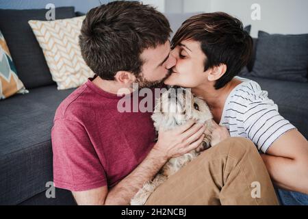 Zärtliches Paar küsst sich, während es zu Hause mit einem Mischlingshund sitzt Stockfoto
