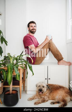 Ein mittelerwachsener Mann schaut weg, während er mit einem Mischlingshund zu Hause sitzt Stockfoto