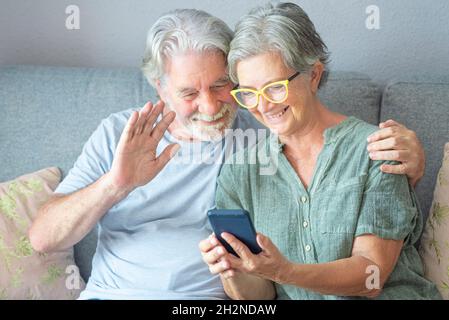 Älterer Mann winkt während eines Videoanrufs über das Smartphone, während er zu Hause bei einer Frau sitzt Stockfoto