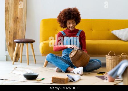 Rotschopf Frau Polieren Korbkorb, während zu Hause sitzen Stockfoto