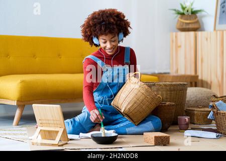 Frau trägt Kopfhörer und malt Korbkorb im Wohnzimmer Stockfoto