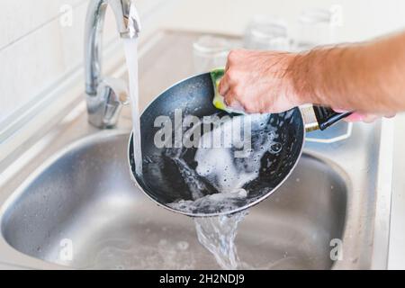 Mann, der die Pfanne am Waschbecken in der Küche putzte Stockfoto