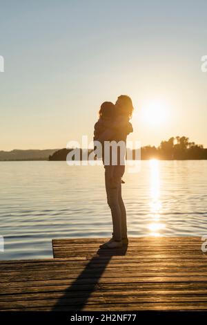 Mutter trägt Tochter, während sie am Wochenende auf dem Meer steht Stockfoto