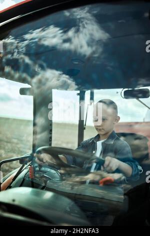 Boy fährt Traktor durch Glas im Fieldd gesehen Stockfoto