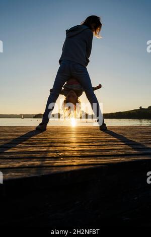 Mutter und Tochter spielen während des Sonnenuntergangs am Pier Stockfoto