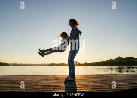 Mutter hebt und dreht Mädchen am Pier während des Wochenendes Stockfoto