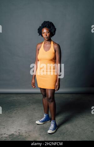 Selbstbewusste junge Frau in orangefarbenem Kleid vor grauem Hintergrund Stockfoto