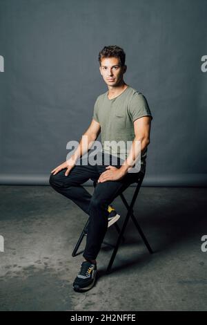 Junger Mann sitzt auf einem Stuhl im Studio Stockfoto