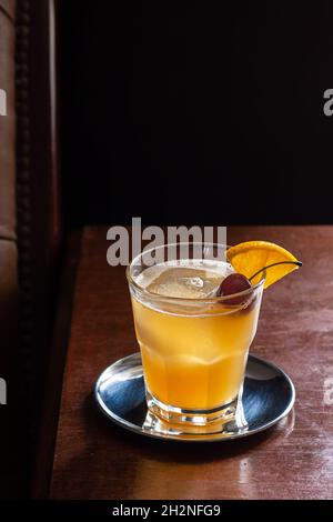 Amaretto Sour Cocktail Drink on the Rocks mit Orangen- und Kirschkrisen in der dunklen, luxuriösen Bar Stockfoto