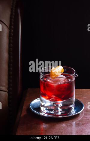 Negroni Cocktail mit Orange Twist in Rocks Glass in einer dunklen luxuriösen Bar mit Copy Space Stockfoto