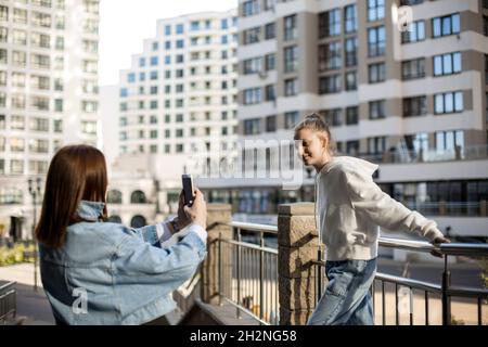 Mutter fotografiert Tochter, die am Geländer durch das Smartphone steht Stockfoto