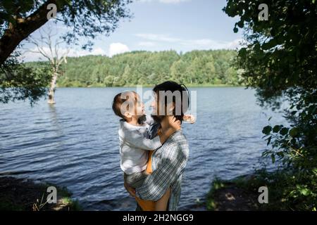 Vater schaut Sohn an, während er am See im Wald steht Stockfoto