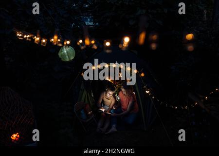 Enkelin mit digitalem Tablet beim Camping mit Großmutter im Hinterhof Stockfoto