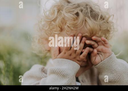 Niedlicher Junge, der die Augen mit den Händen bedeckt Stockfoto