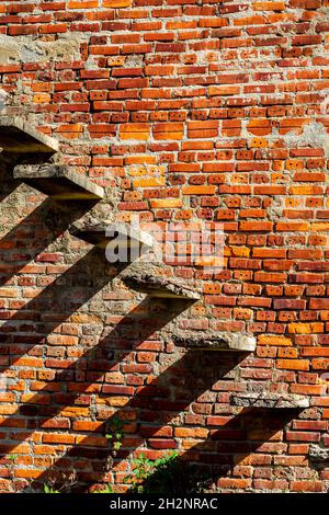 Zementtreppen, die aus der Ziegelseite eines Gebäudes in Ruinen kommen. Nur Schritte und Schatten. Stockfoto