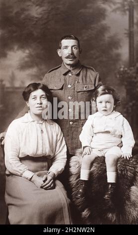 Ein Porträt eines britischen Soldaten aus der Zeit des Ersten Weltkriegs, der stolz mit seiner Frau und seinem jungen Kind posiert. Er hat ein Medaillenband, das für die Army Long Service and Good Conduct Medal oder Territorial Efficiency Medal sein könnte. Aufgenommen in Winchester, Großbritannien. Stockfoto