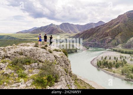 Eine Familie bewundert den Gebirgsfluss, während sie am hohen, steilen Ufer am Zusammenfluss der Flüsse Katun und Chuya in der Altai-Republik steht Stockfoto
