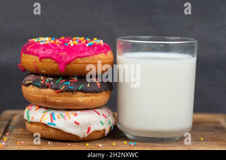 Schönes, süßes Essen. Stapel von glasierten bunten verschiedenen Donuts mit einer Tasse Milch auf einem grauen Hintergrund. Stockfoto