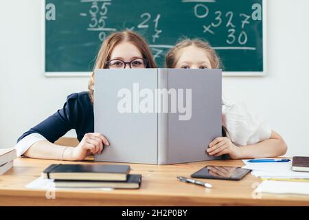 Schülerinnen, die sich hinter Büchern verstecken, sitzen in einem Klassenzimmer. Stockfoto