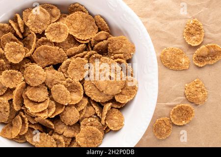 Natürliche mehrkörnige Flocken in einer weißen Keramikplatte auf braunem Papier, Nahaufnahme, Draufsicht. Stockfoto