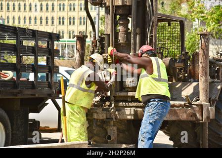 Zwei afroamerikanische Bauarbeiter bohren sicher ein Loch im Stadtzentrum, das an den Wisconsin River, Urban Renewal, Milwaukee, Wisconsin, USA, angrenzt. Stockfoto