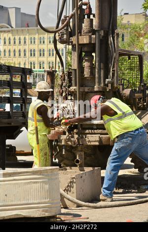 Zwei afroamerikanische Bauarbeiter bohren sicher ein Loch im Stadtzentrum, das an den Wisconsin River, Urban Renewal, Milwaukee, Wisconsin, USA, angrenzt. Stockfoto