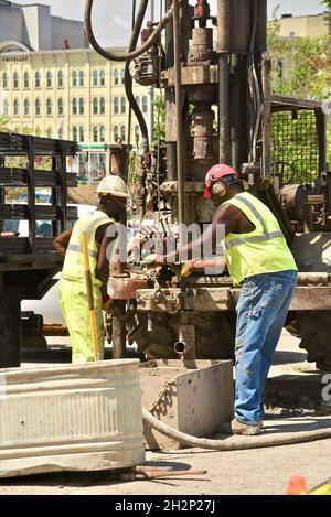 Zwei afroamerikanische Bauarbeiter bohren sicher ein Loch im Stadtzentrum, das an den Wisconsin River, Urban Renewal, Milwaukee, Wisconsin, USA, angrenzt. Stockfoto