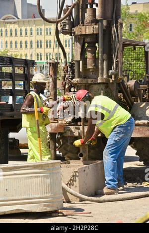 Zwei afroamerikanische Bauarbeiter bohren sicher ein Loch im Stadtzentrum, das an den Wisconsin River, Urban Renewal, Milwaukee, Wisconsin, USA, angrenzt. Stockfoto