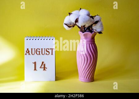 Kalender mit Text 14. august auf gelbem Hintergrund und mit Blumenvase Stockfoto