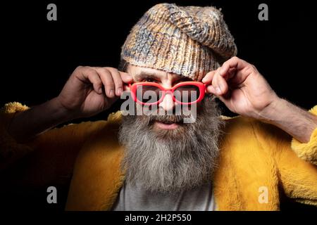 Modischer älterer bärtiger Mann in heller Kleidung auf schwarzem Hintergrund. Stockfoto