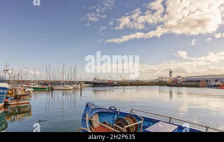 Ein Hafen und Yachthafen mit Yachten und Fischerbooten. In der Ferne befindet sich ein Leuchtturm und im Vordergrund der Bug eines Fischerbootes. Stockfoto
